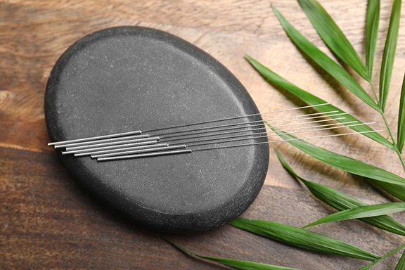 Acupuncture needles, spa stone and leaf on wooden table, flat la